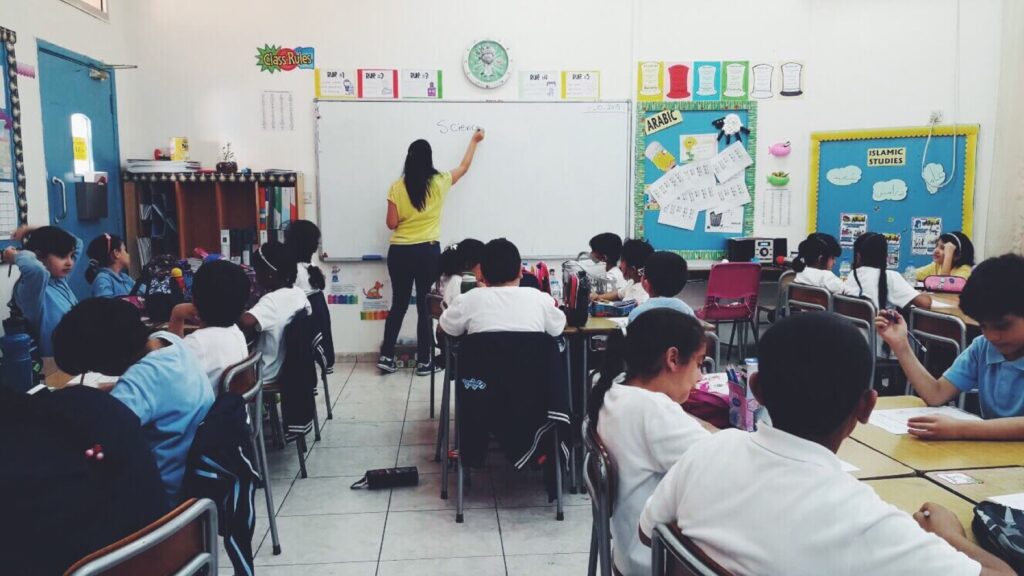 Teacher writing on white board in front of their class