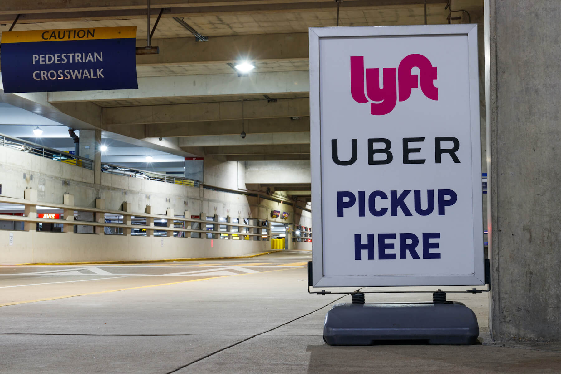 Sign reads "Lyft Uber Pickup Here" in airport parking lot