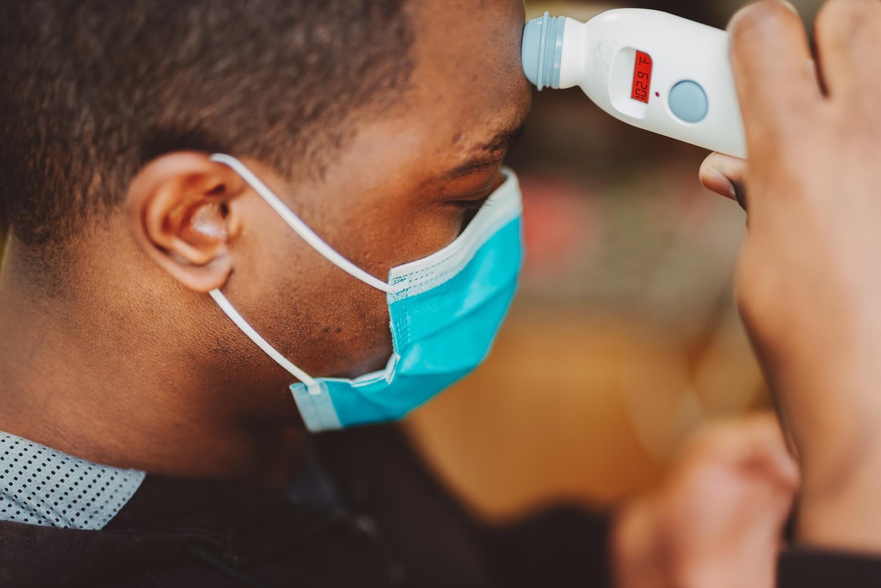 Black man in surgical mask takes his temperature