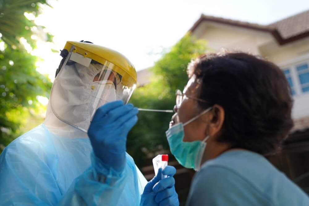 Healthcare worker in PPE administers nasal COVID-19 swab test to elder Asian person