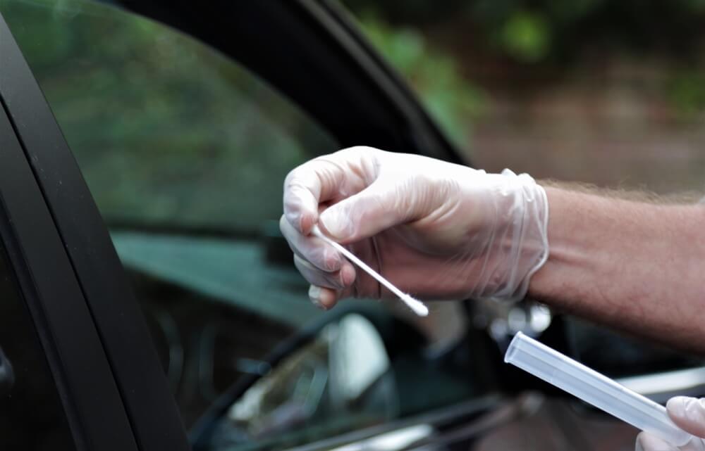 Gloved hand holding nasal swab after COVID-19 test