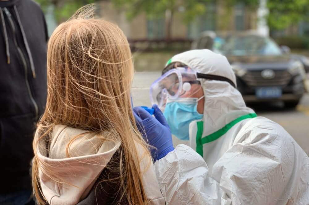 Healthcare worker in PPE administers PPE test to small white child