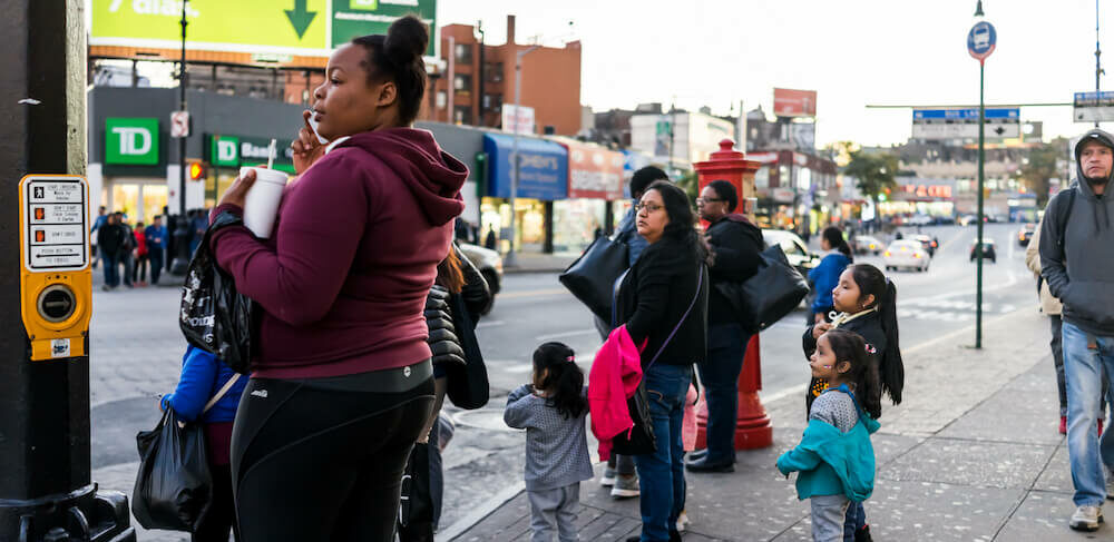 Black and Brown families wait to cross the street at the light in the Bronx, New York