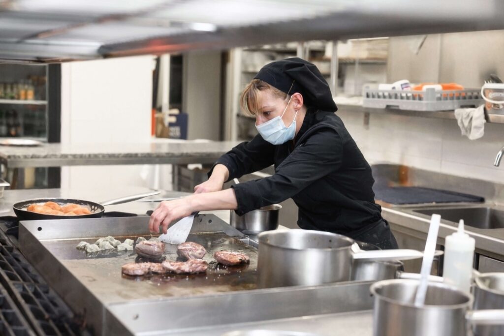 Chef or cook wearing a mask and cooking in an industrial kitchen