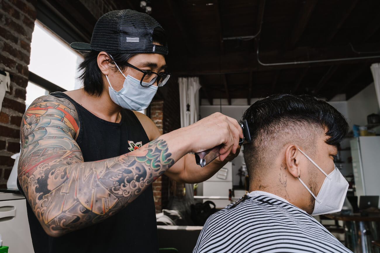 Asian barber in mask cutting hair