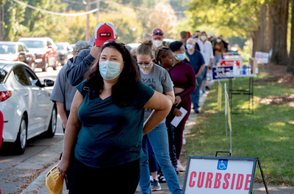 A lady wearing a face mask is amongst a diverse group of voters on the first day of early voting.