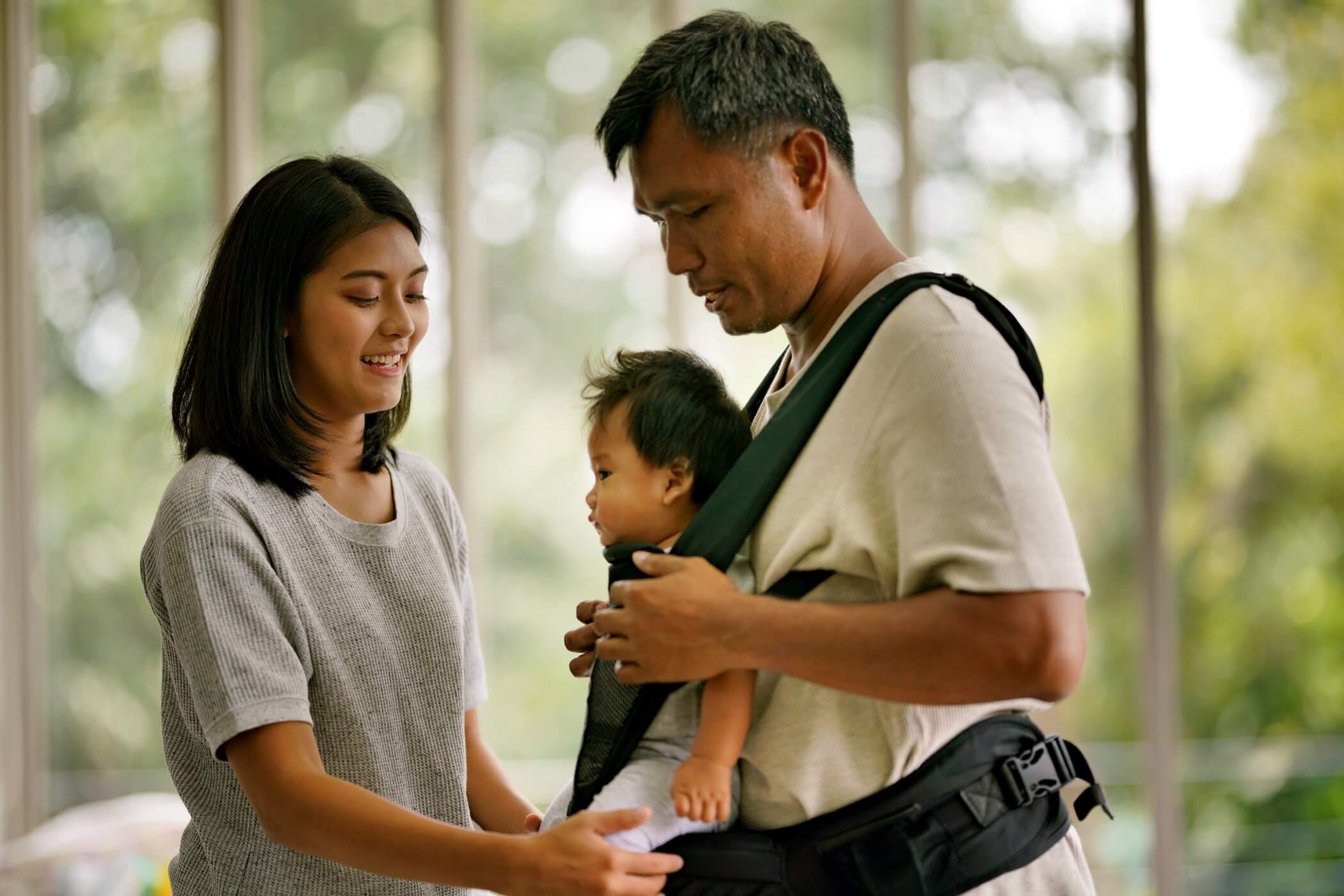 Asian mother and father strap infant into carrier