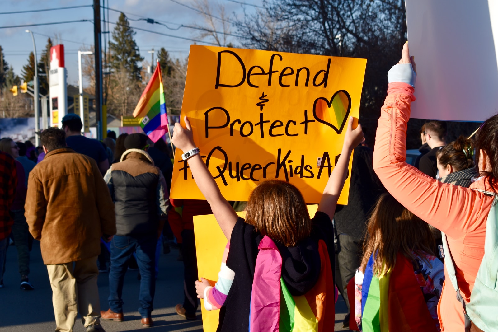 Peoosn holding printed orange paper that reads "Defend + Protect Queer Kids"