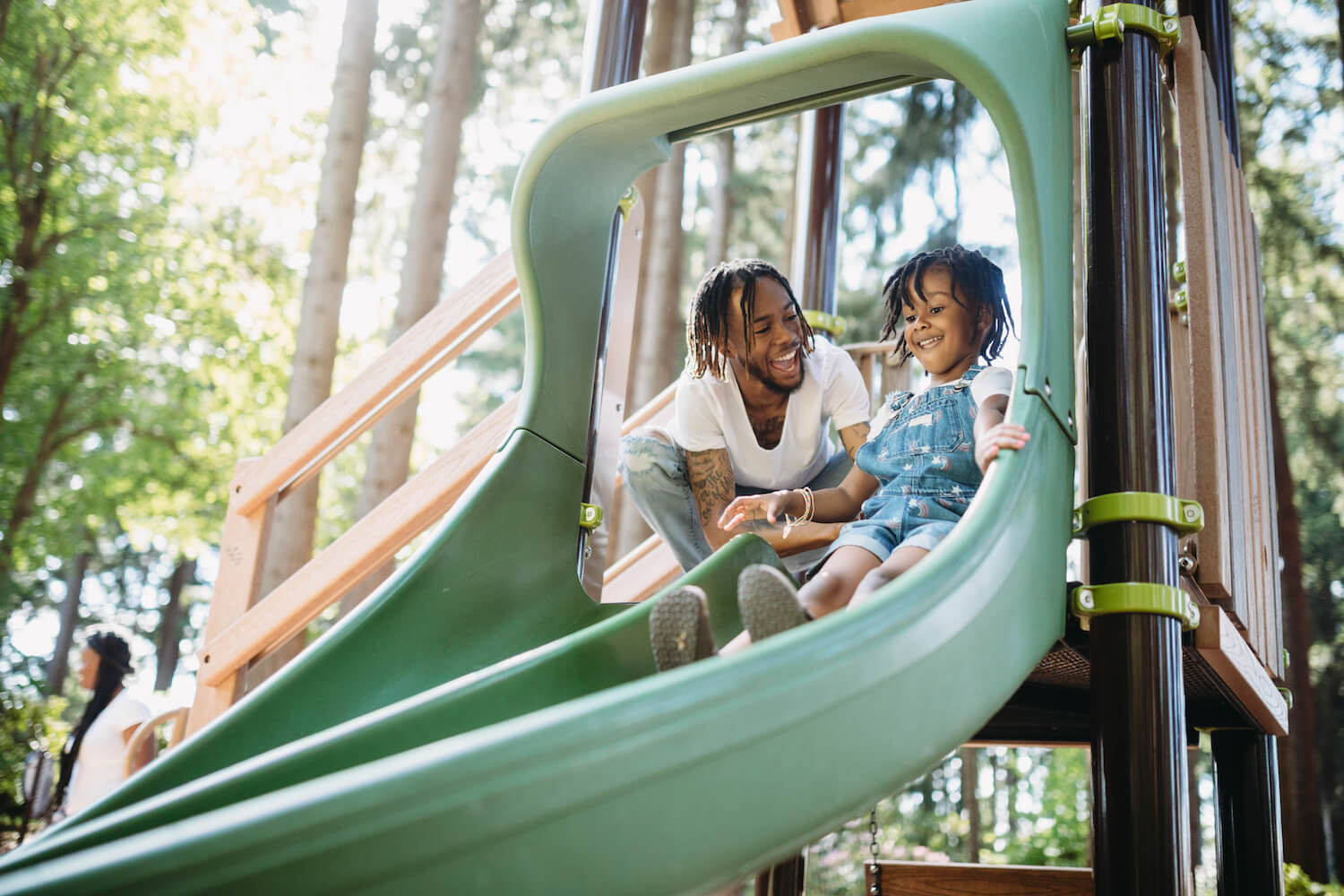 Black father playing with daughter on playground slide