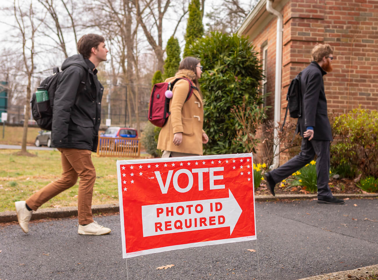 Three white primary election voters arrive at polling place in Arlington Virginia. Sign reads, "Vote. Photo ID Required."