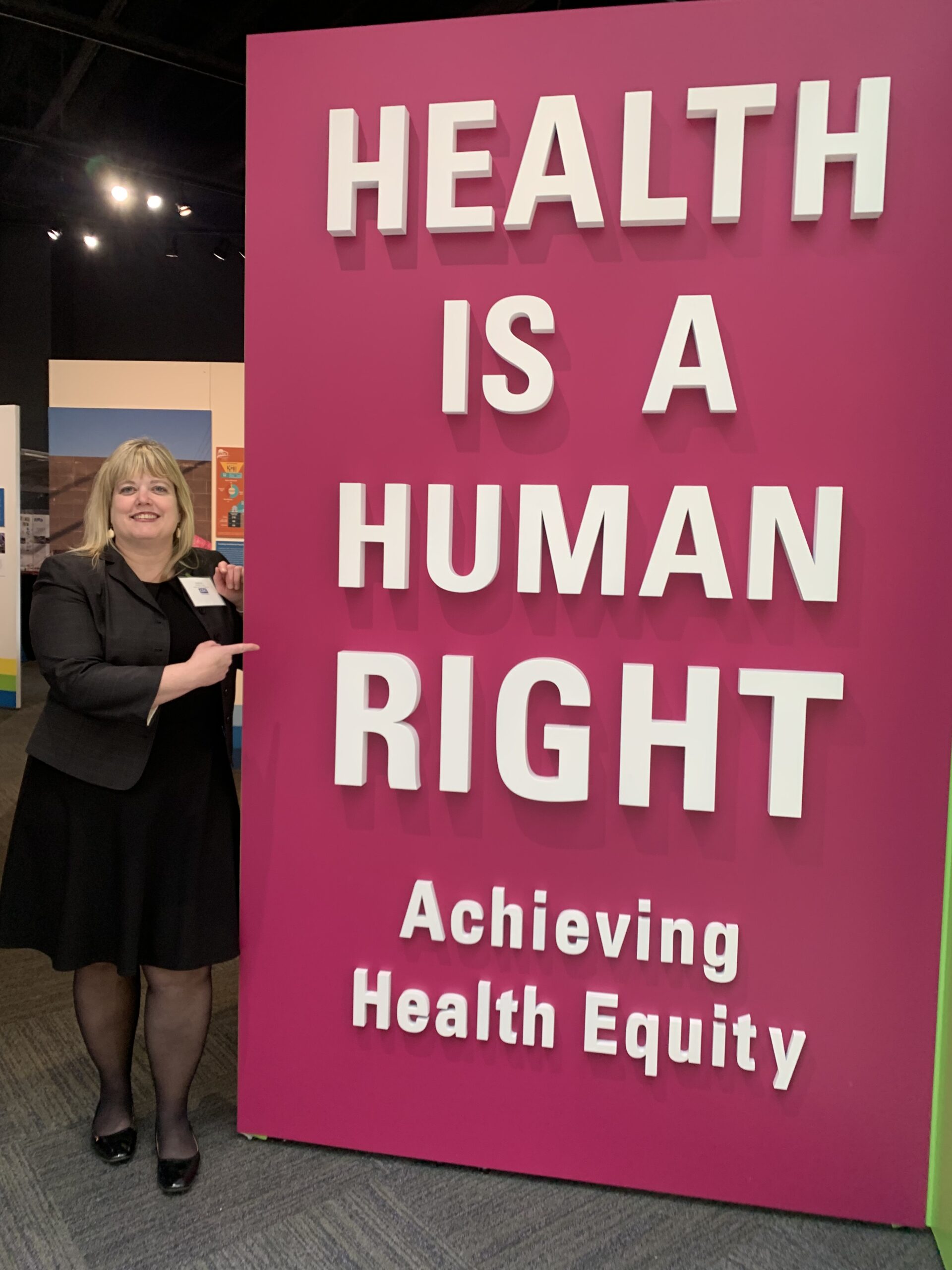 AK Rep. Geran Tarr stands by a sign that reads "Health is a Human Right: Achieving Health Equity"